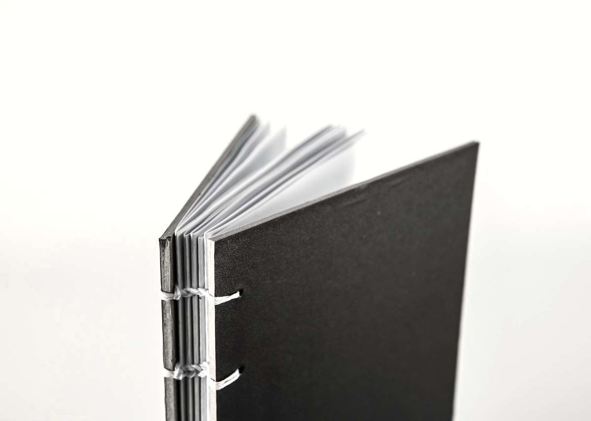 Cuaderno cosido a mano, de tapa negra, sobre fondo blanco
