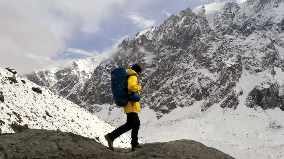 Una persona de espaldas con mochila y chaqueta amarilla sobre una cresta rocosa