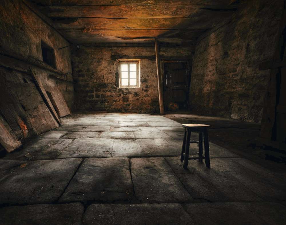 Cuarto de piedra con un taburete bajo una ventana pequeña
