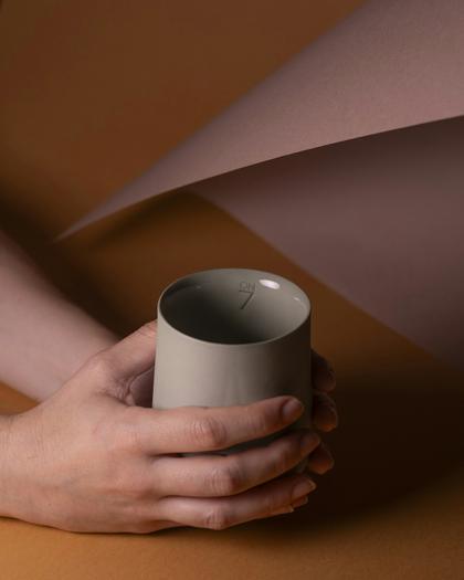 Una taza gris sostenida entre las manos sobre papel ocre