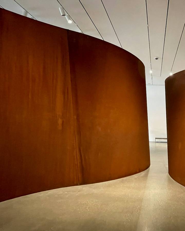 Dos muros de acero oxidado en curva dentro de una sala luminosa