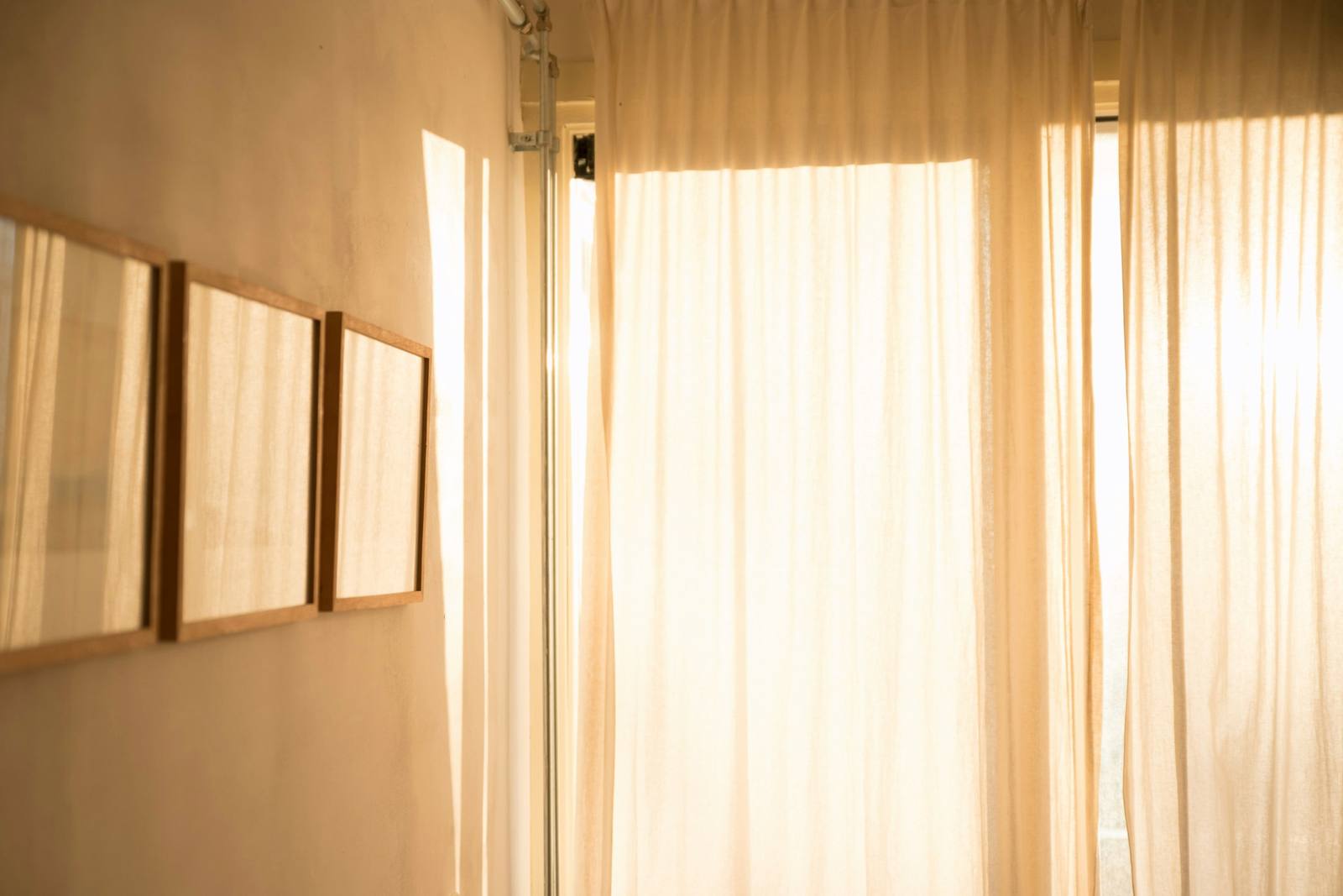 Cortinas de lino con la luz del atardecer y tres marcos sobre un muro cálido