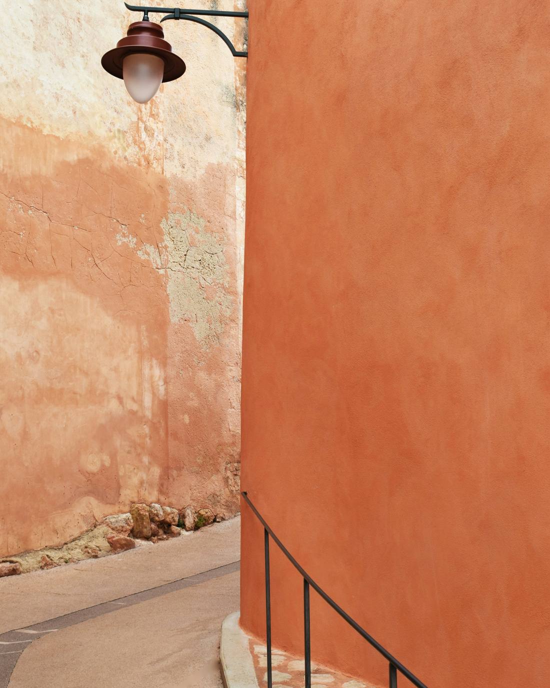 Muro curvo color terracota con una lámpara de hierro