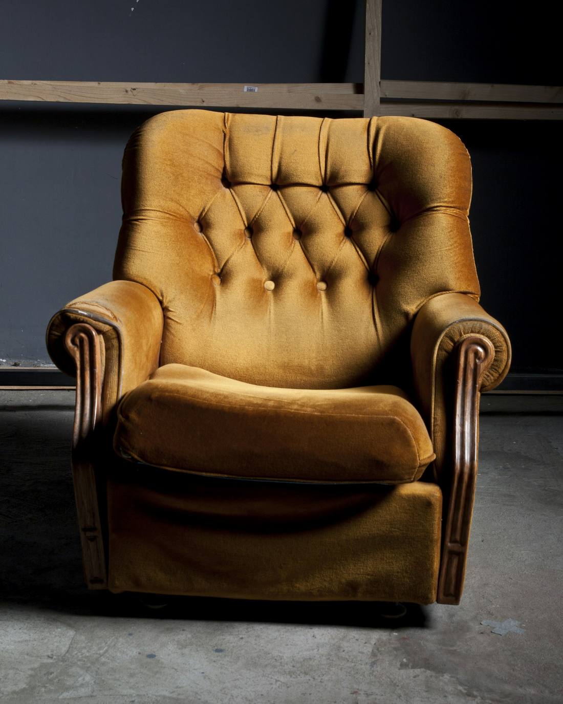 Sillón de terciopelo ocre con capitoné sobre un suelo de cemento
