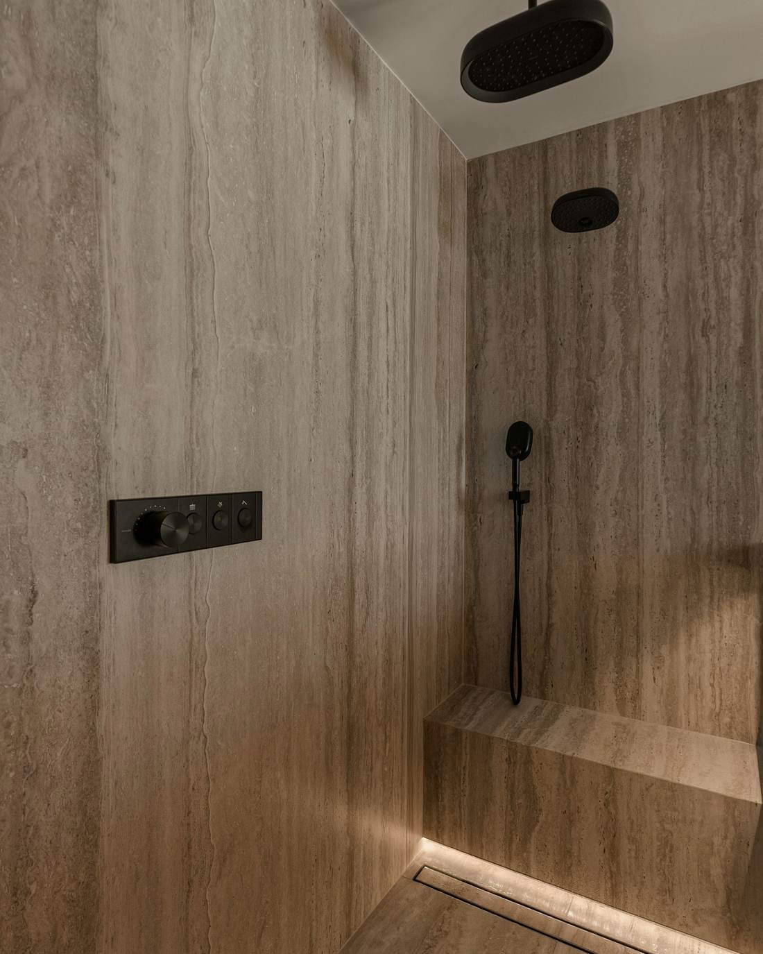 Ducha revestida de travertino con una línea de luz en el suelo