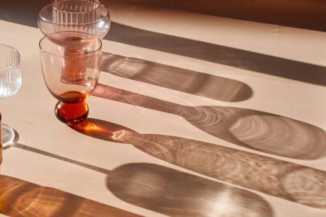 Vasos y copas de vidrio ámbar y transparente con sus sombras sobre una mesa rosada