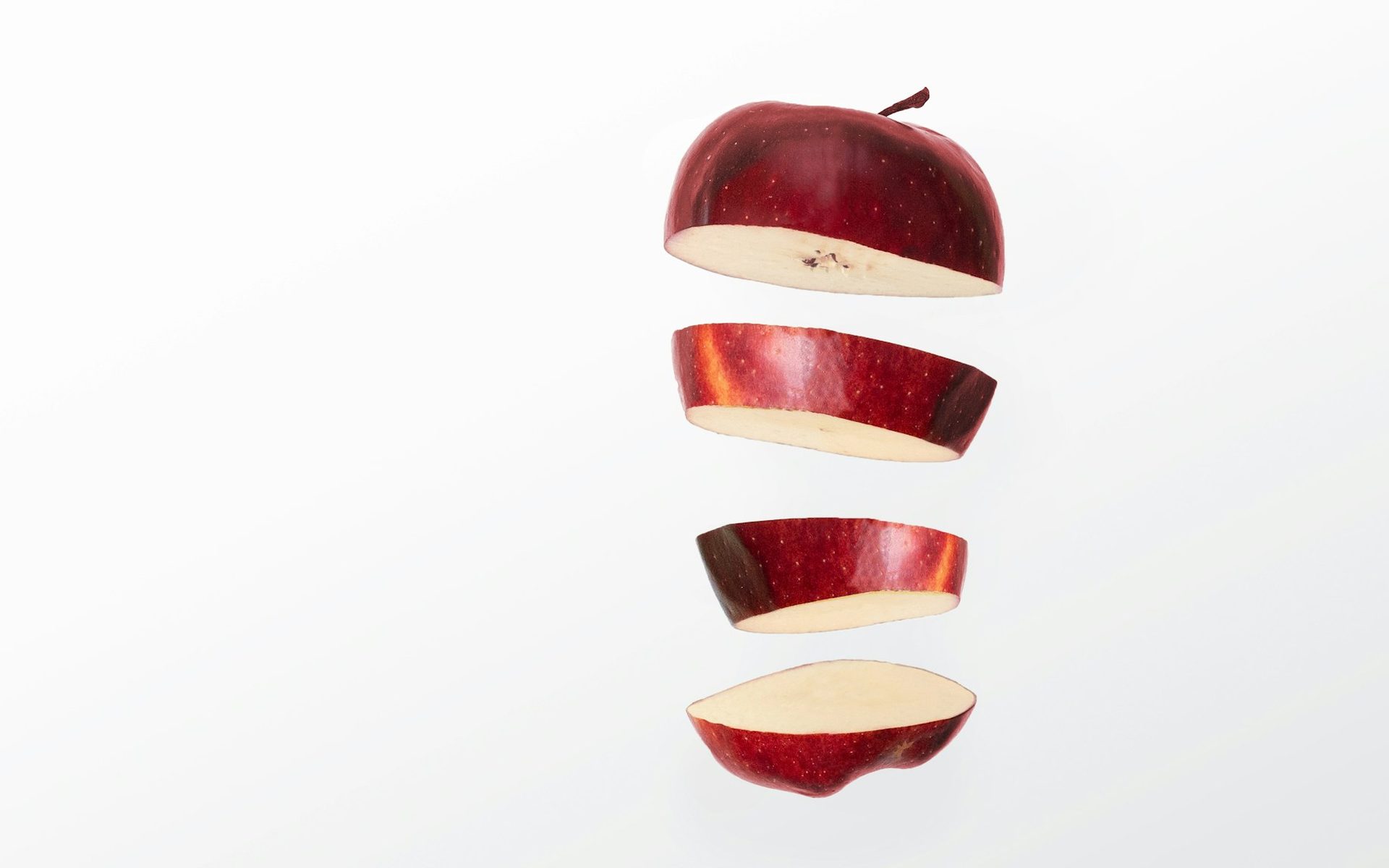Una manzana roja en rodajas suspendida sobre un fondo blanco