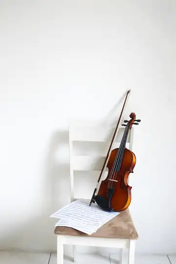 Violín apoyado en una silla blanca, con una partitura sobre el asiento