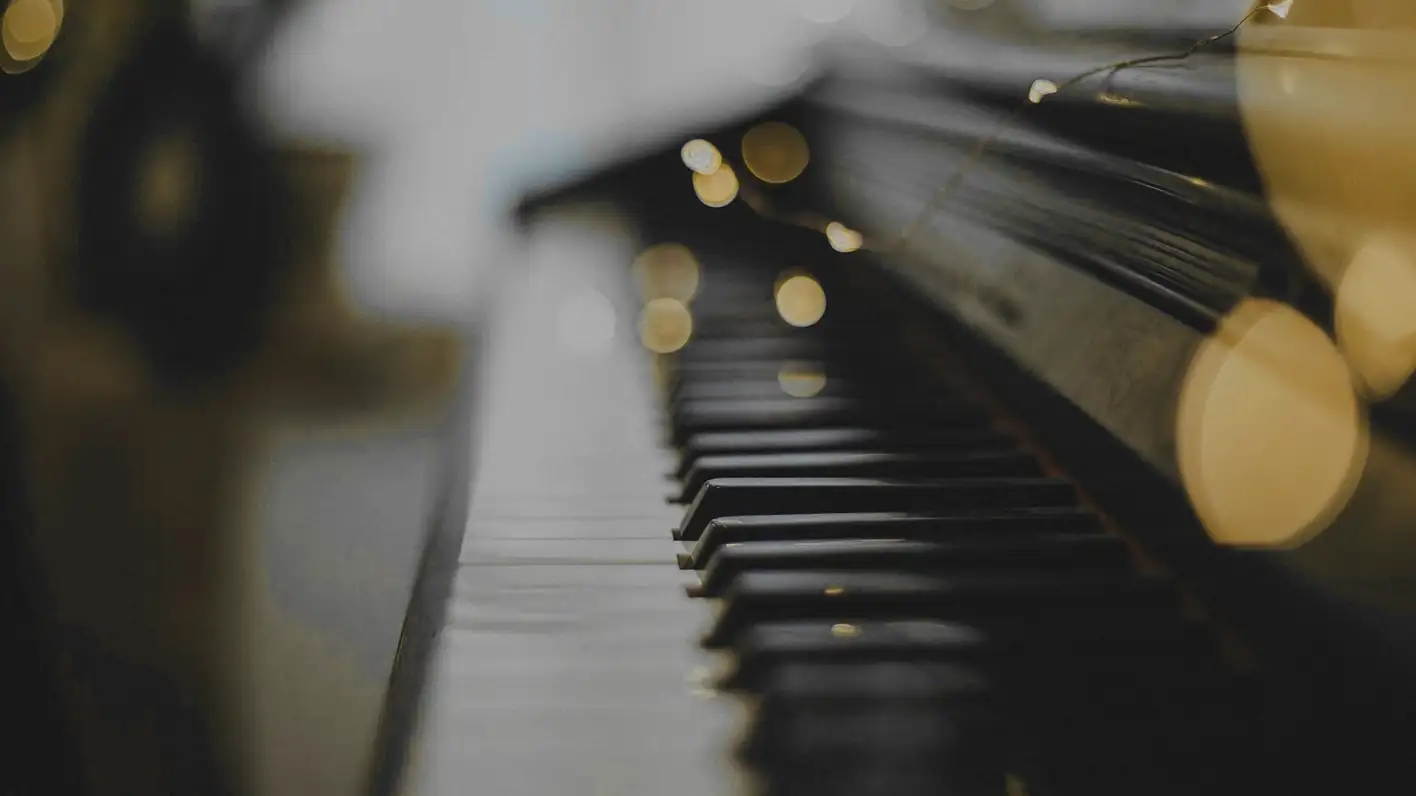 Teclado de piano desenfocado, con luces cálidas al fondo