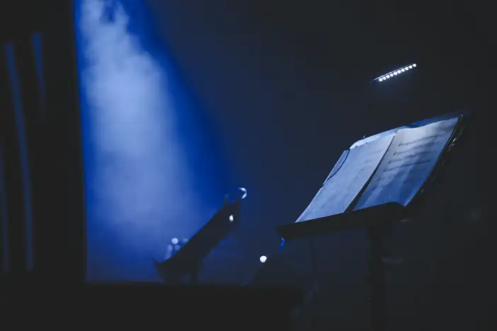 Atril con una partitura iluminada por una luz azul, en una sala en penumbra