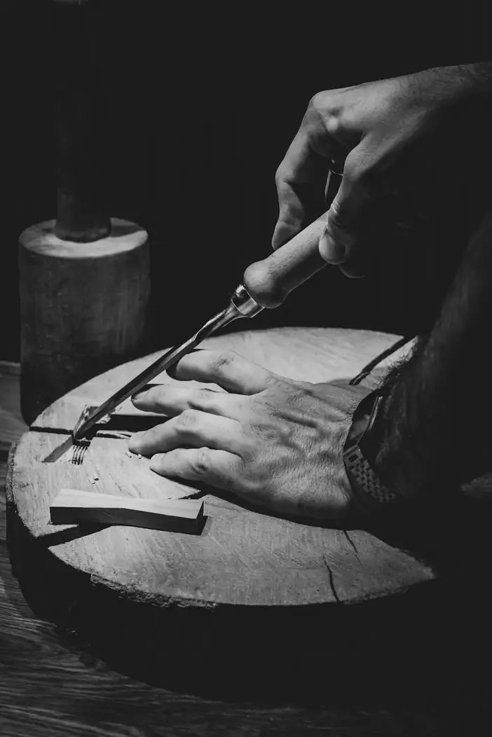 Manos que tallan una pieza de madera, en blanco y negro